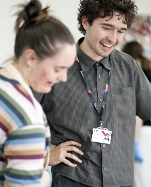 Two people discussing artwork in a studio, with others working in the background. Two people discussing artwork in a studio, with others working in the background.